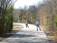 Rollerblading on a sunlit, winding paved trail through late-winter woods.